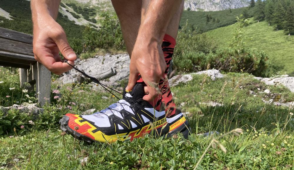 Sportista veže trail running patike na planinskoj stazi tokom ljetnog outdoor treninga u prirodi.